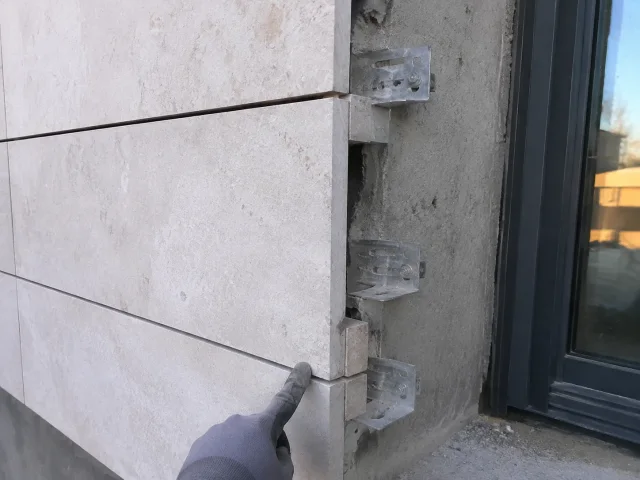 Stone cladding ends beside a window, leaving the concrete reveal and fixing brackets exposed